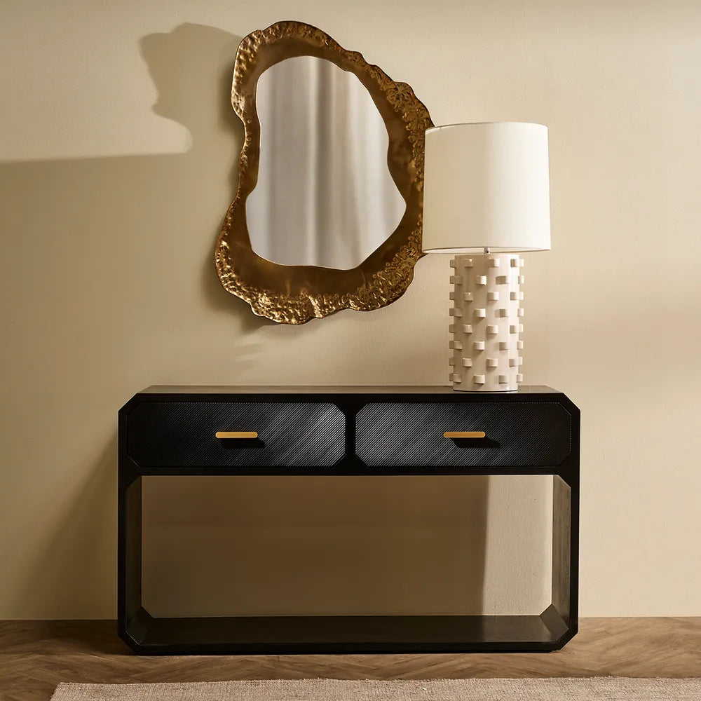 Decorative console table with a lamp and mirror on a beige wall.