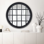 Round mirror with black frame on a white wall above a white console table.