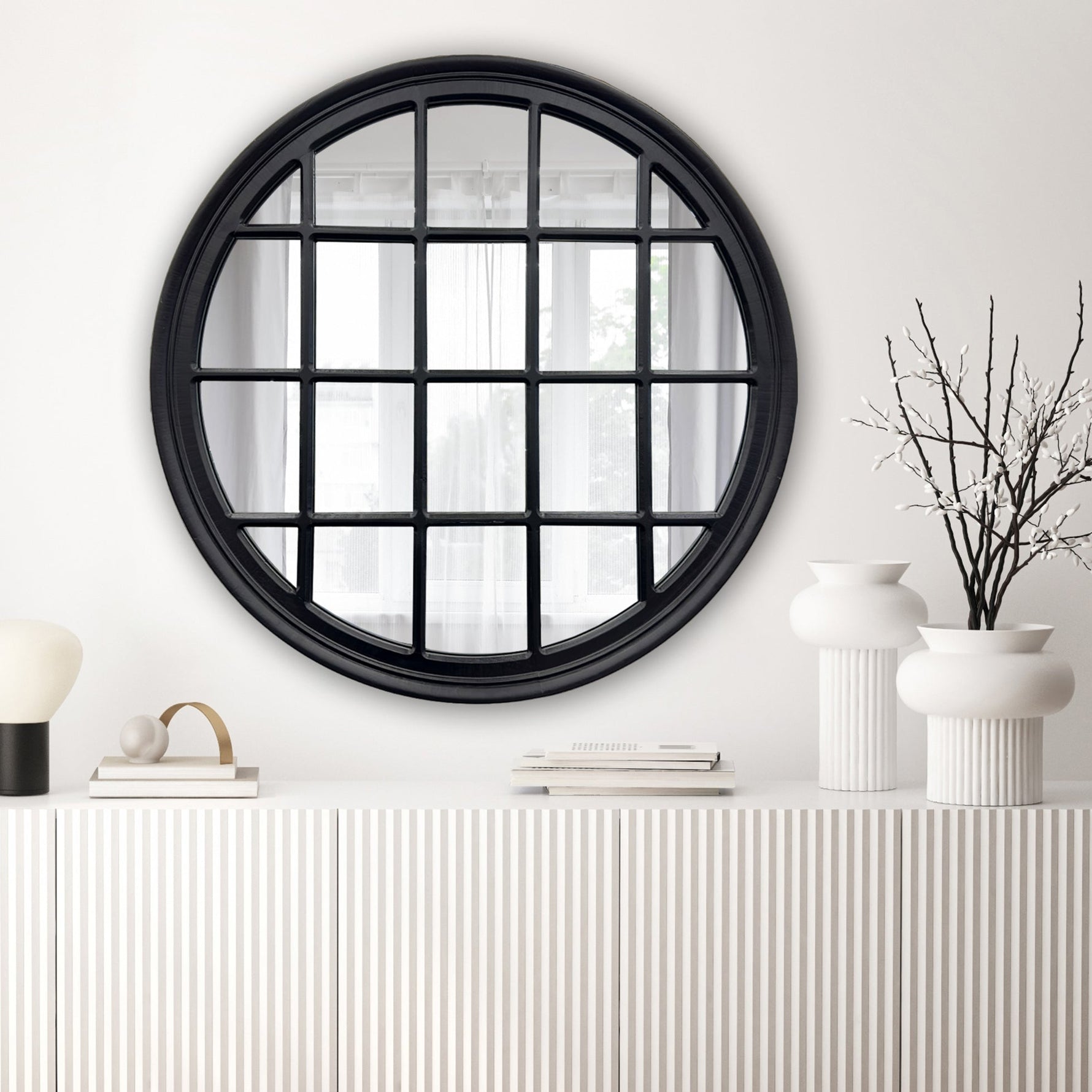 Round mirror with black frame on a white wall above a white console table.