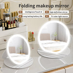 Folding makeup mirror with LED lights on a vanity table with cosmetic products.